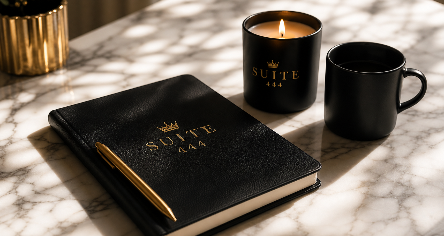 Suite 444 branded notebook, candle, and gold pen on marble.